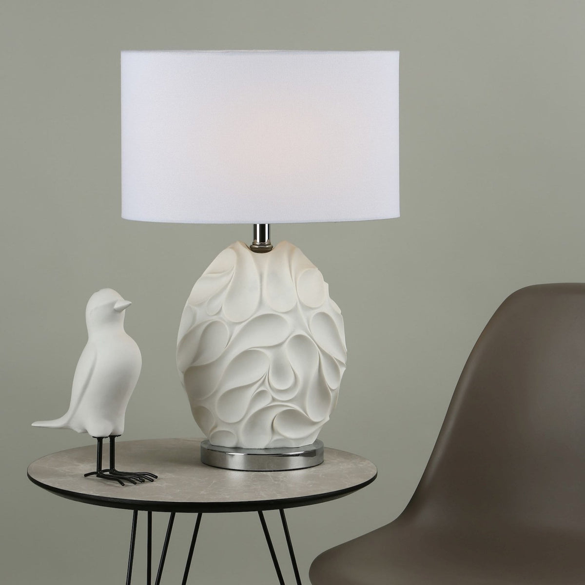 White ceramic table lamp with a textured base and a white rectangular shade, next to a white bird figurine.