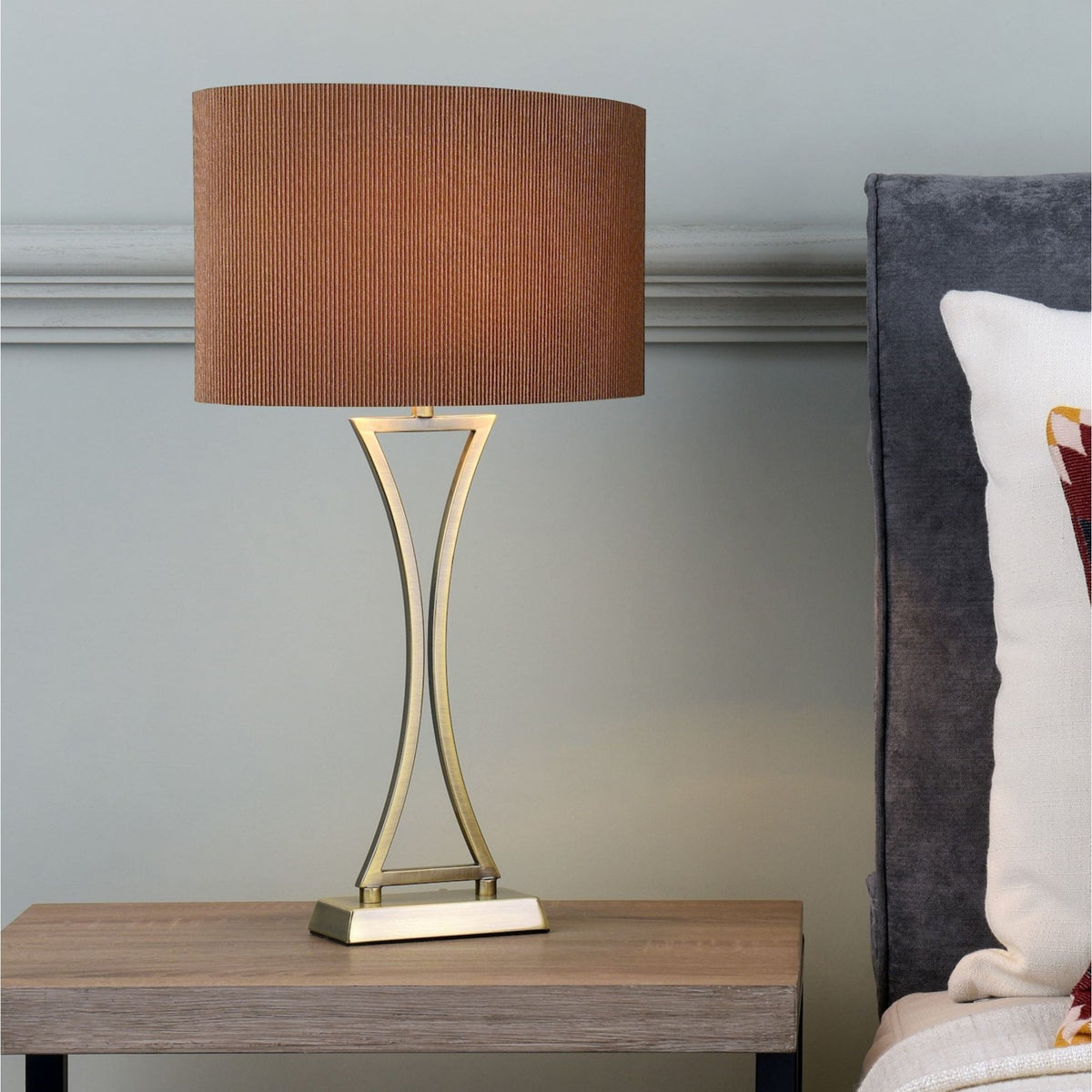 Table lamp with a brown pleated shade and a gold hourglass-shaped base on a wooden nightstand.