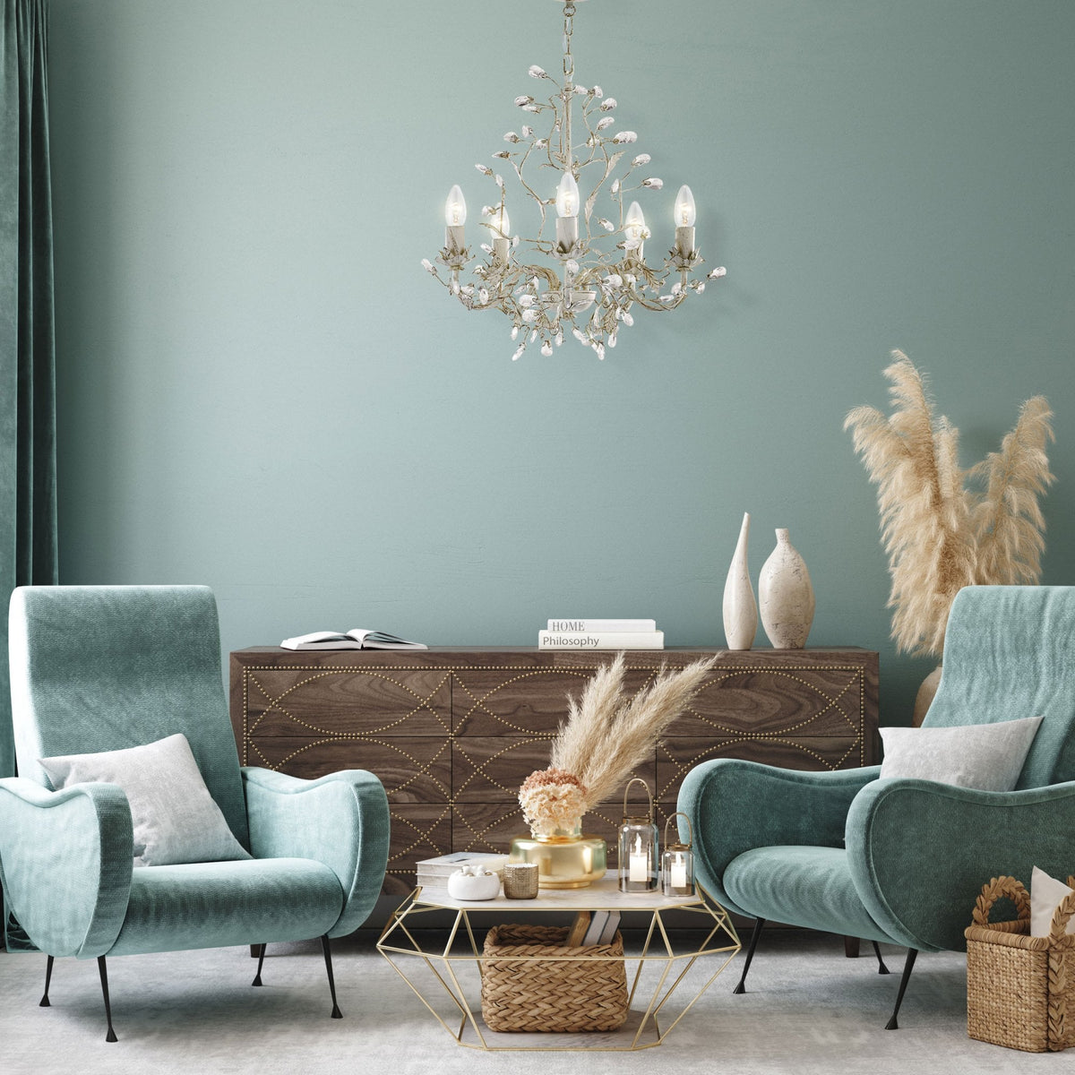 A living room with a white chandelier, two teal armchairs, a wooden cabinet, and decor.