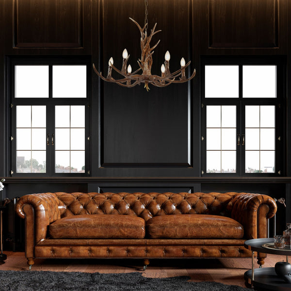 Antler chandelier above a brown leather Chesterfield sofa in a dark room.
