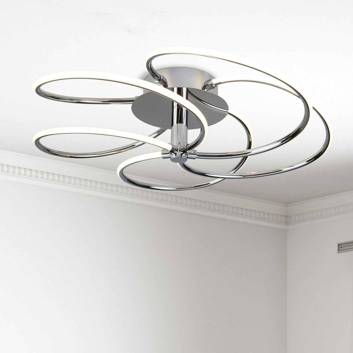 A modern chrome ceiling light with intertwined LED rings against a white ceiling.