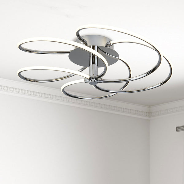 A modern chrome ceiling light with intertwined LED rings against a white ceiling.