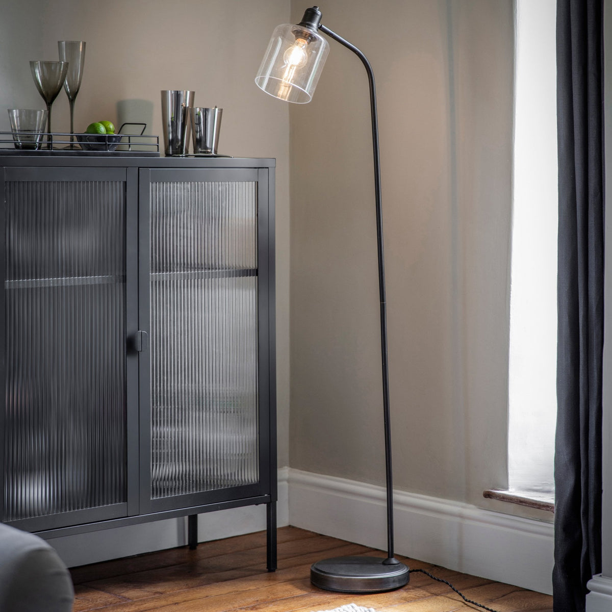 A black metal cabinet with reeded glass doors, next to a black floor lamp with a clear glass shade.