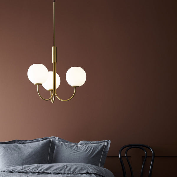 A brass chandelier with three spherical glass shades illuminates a bedroom.
