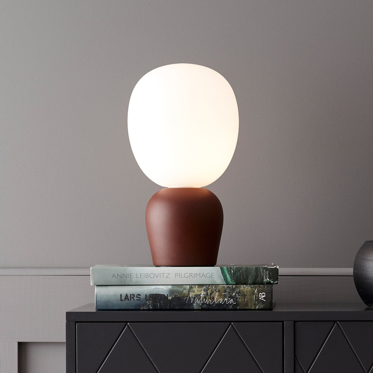 BELID Buddy Table Lamp in Rust with a white globe shade and rust-colored base on a black cabinet