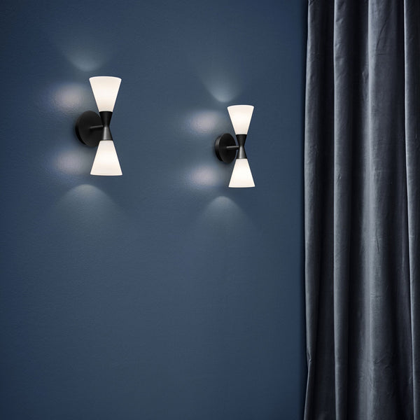 Two modern wall lights with hourglass design on a dark blue wall with a grey curtain.