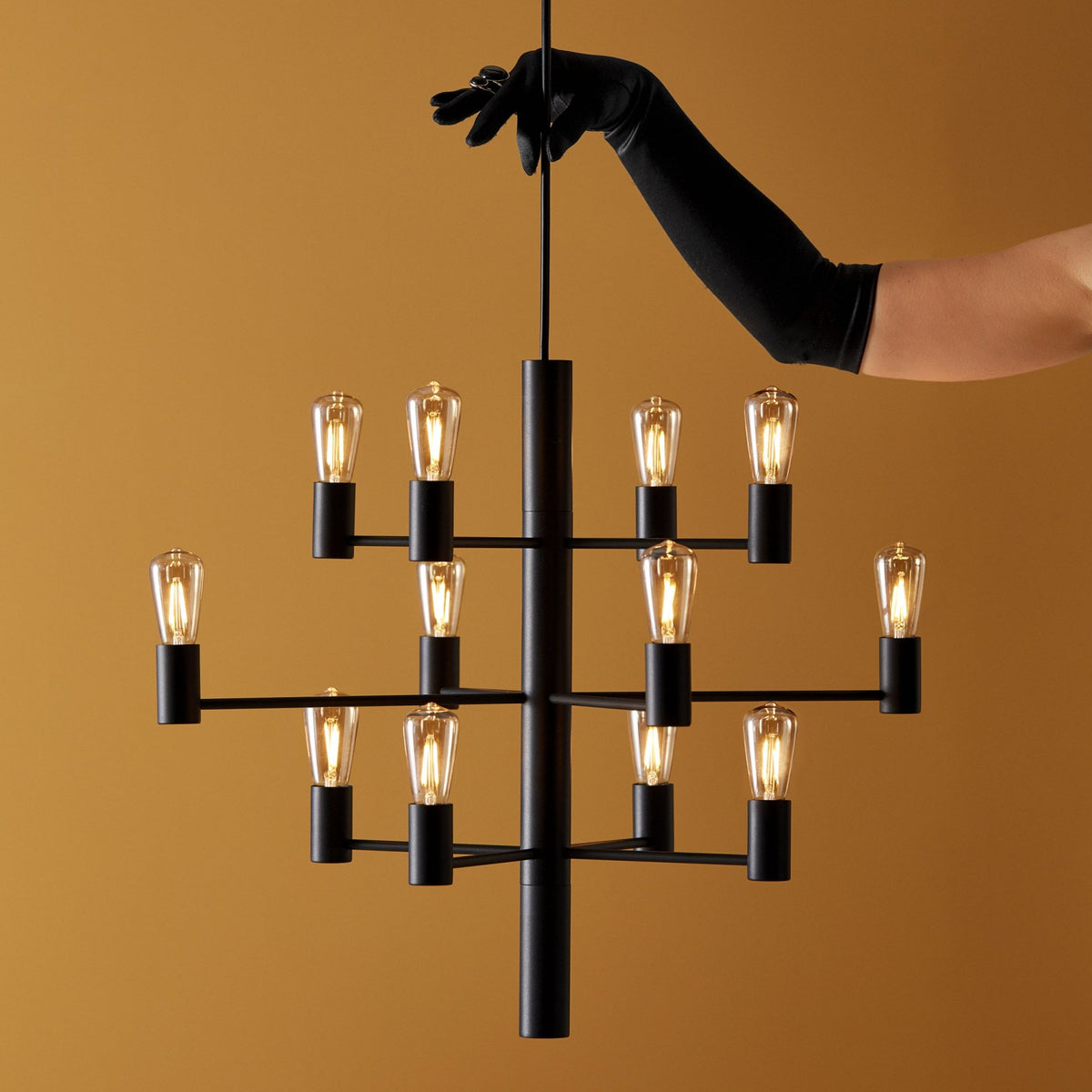 A person in an elegant black glove adjusting a stylish black chandelier with exposed bulbs.