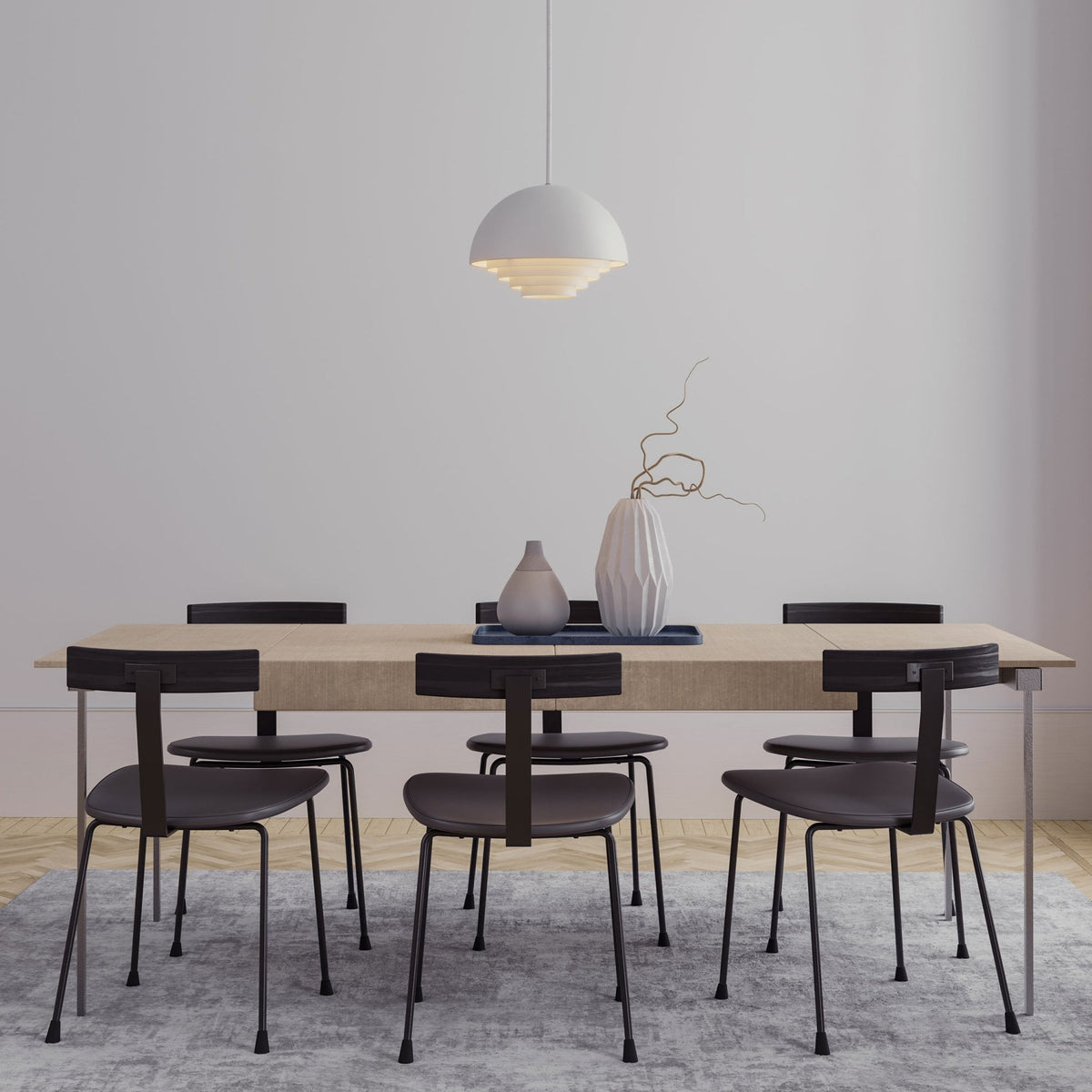 A dining room featuring a light wood table, grey chairs, and a white pendant light.