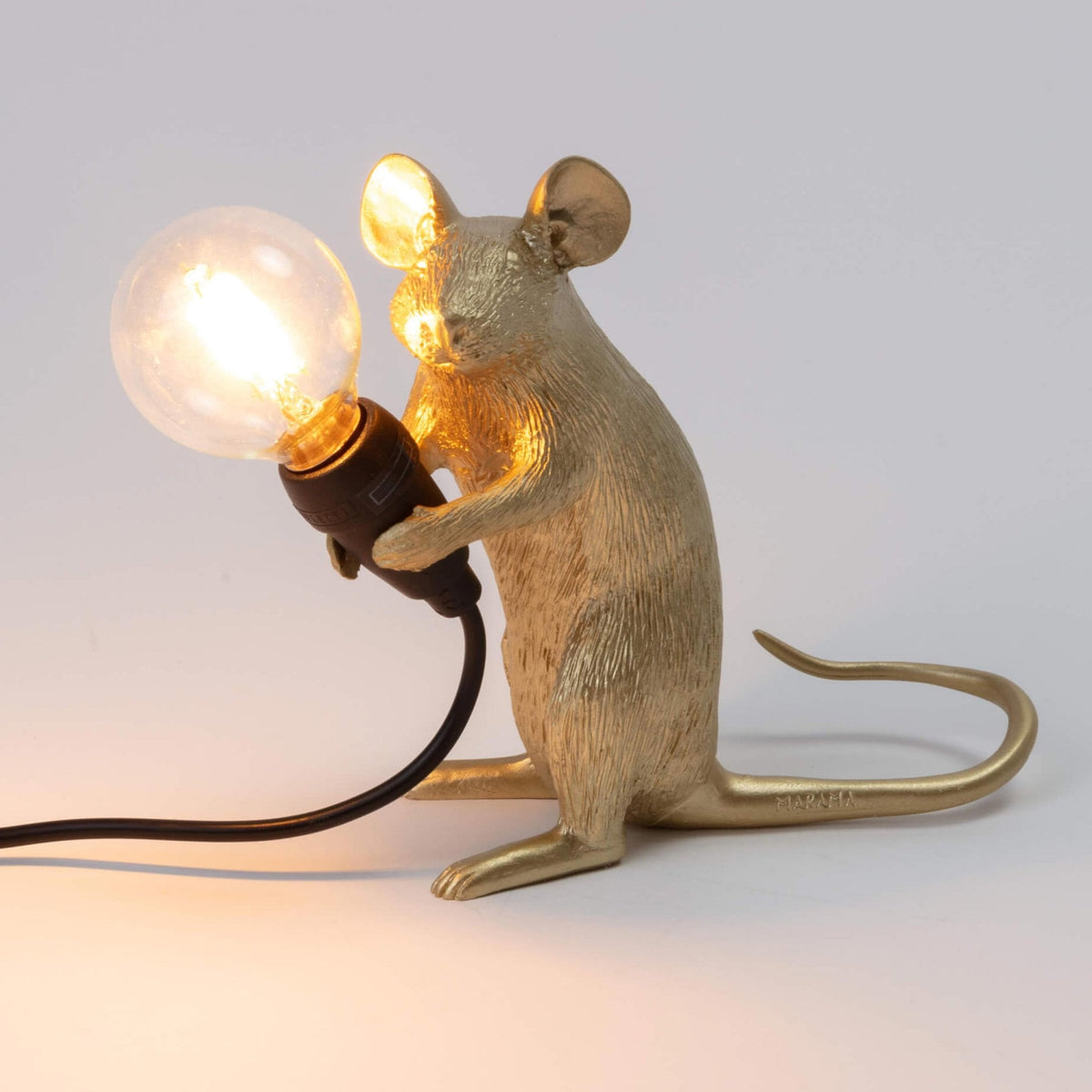 A golden mouse lamp holding a lit bulb, viewed from the front right side.