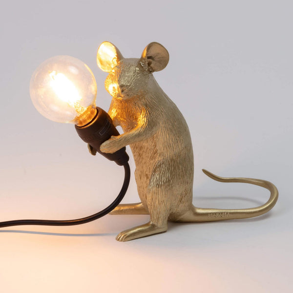A golden mouse lamp holding a lit bulb, viewed from the front right side.
