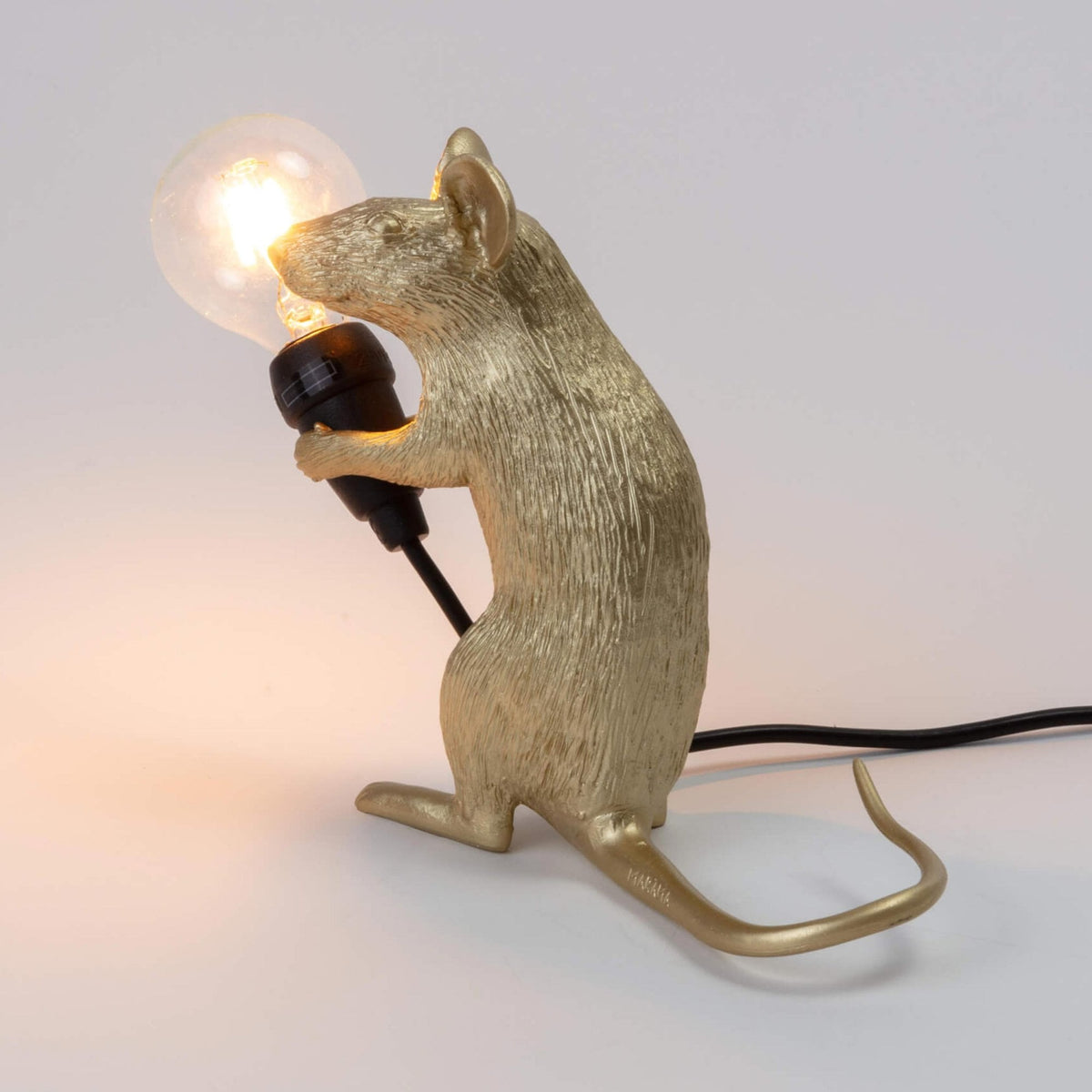 A golden mouse lamp holding a lit bulb, viewed from the front left side.