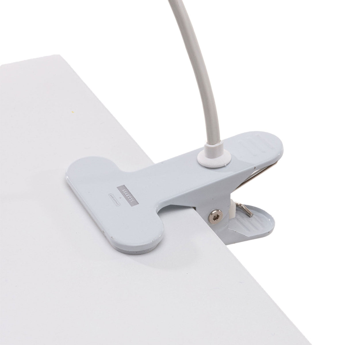 Close-up of a white clip securing the lamp's flexible arm to a white table edge.