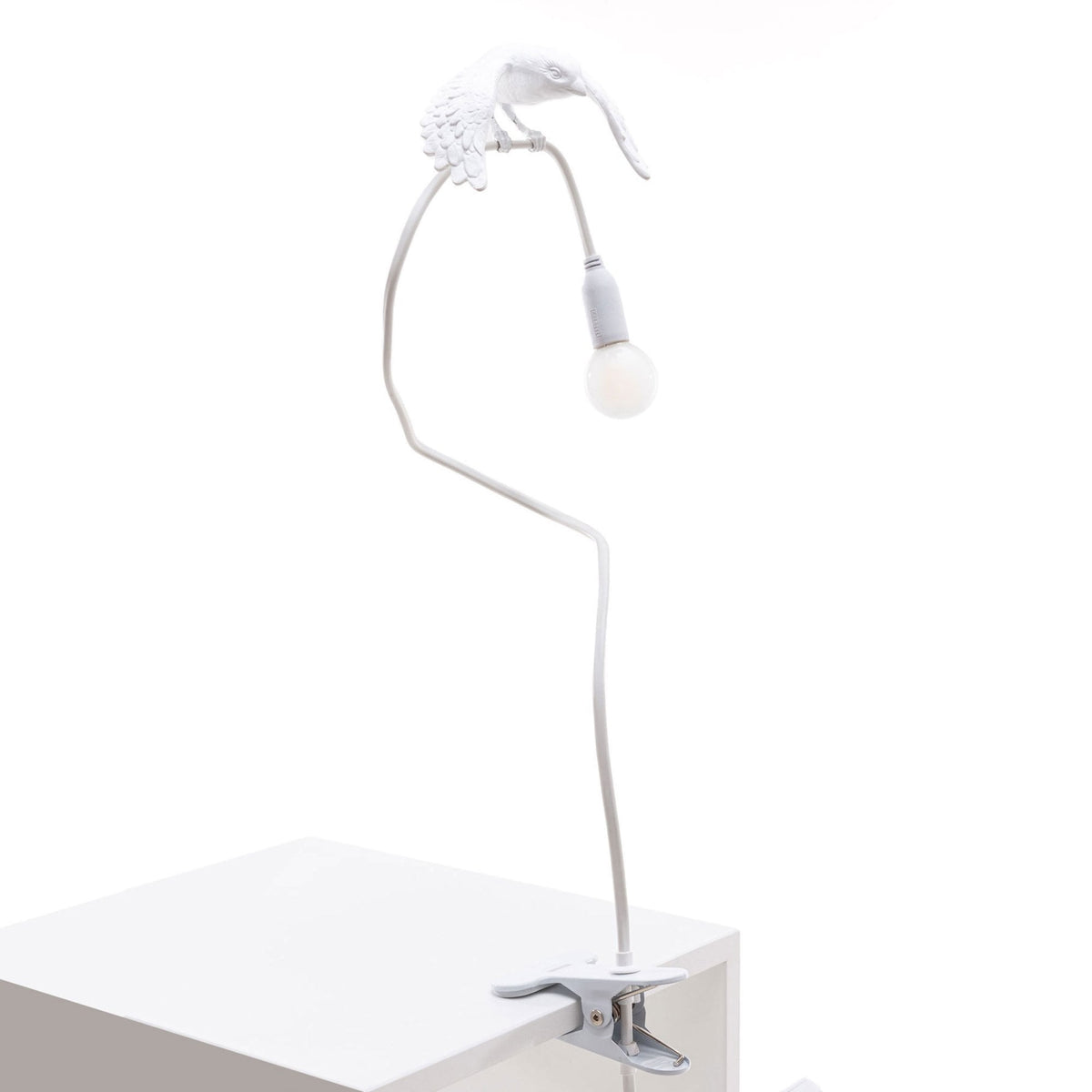 Stylised white bird lamp with a glowing bulb, on a flexible arm, clipped to a white surface.