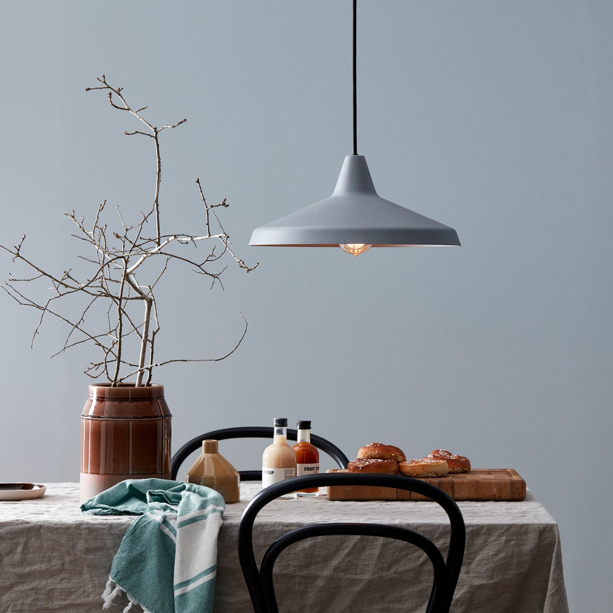BELID Titan Pendant in Concrete Grey hanging above a dining table with food and decor