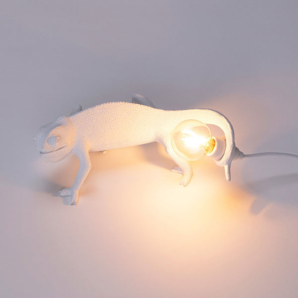 White chameleon lamp holding a glowing bulb, casting a warm light.