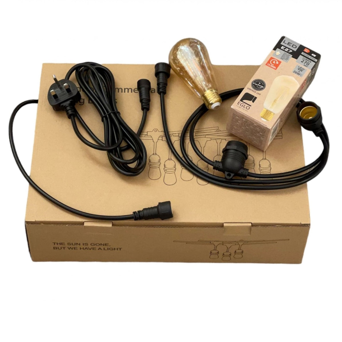 A close up of a box with warm outdoor festoon lights, plug, and a light bulb.