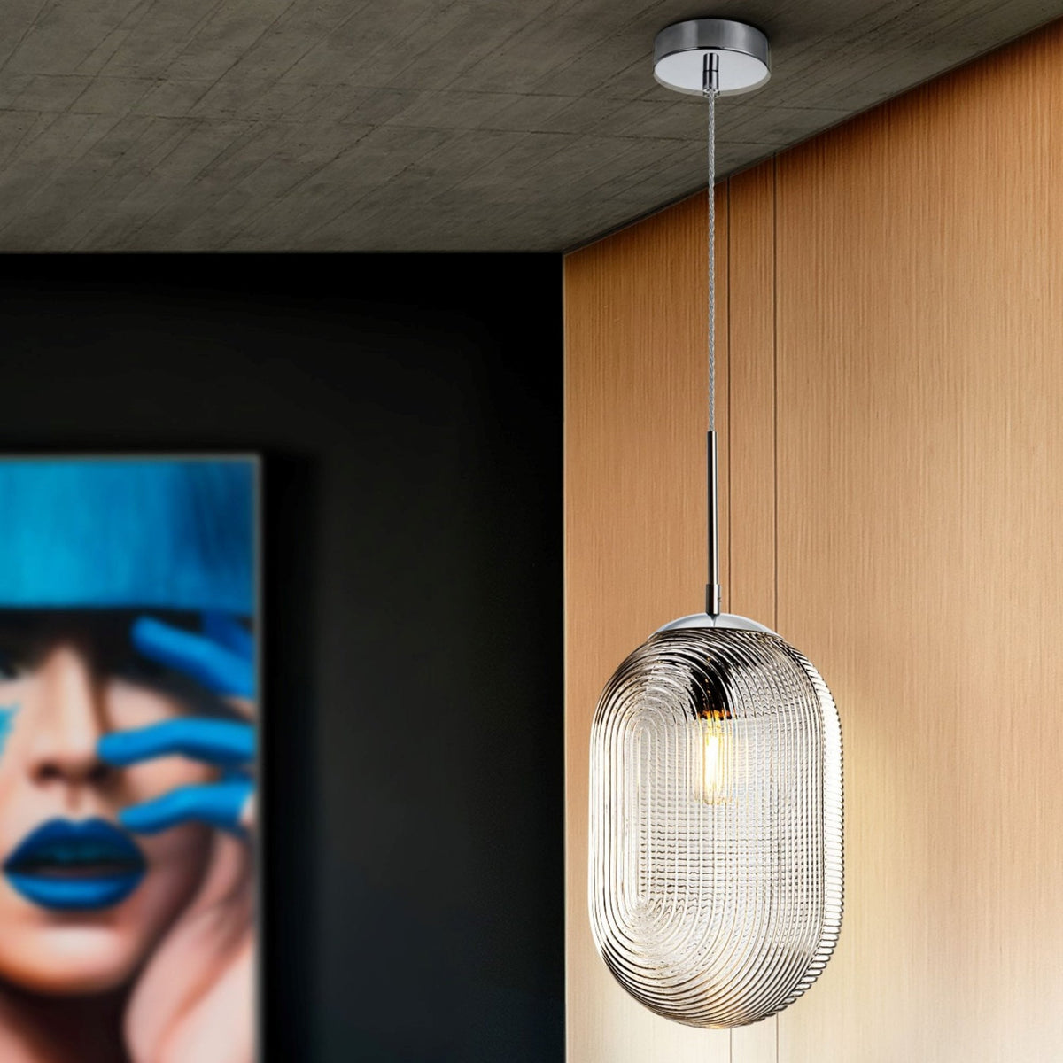 A glass pendant light hanging from a ceiling, with a painting of a person with blue lips in the background.