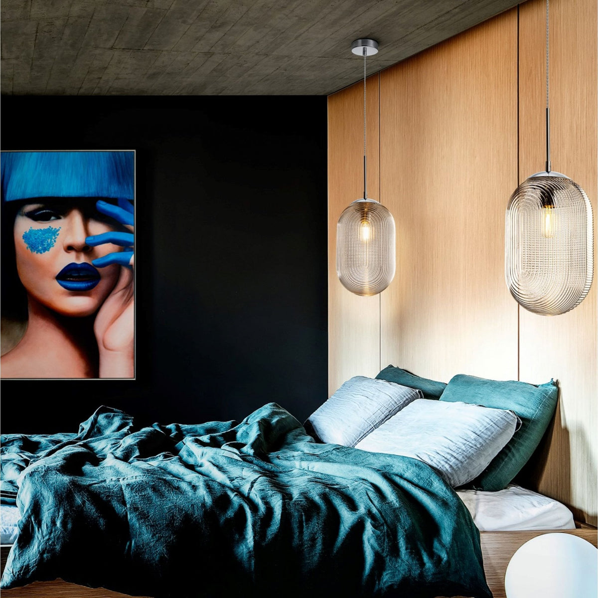 Two smoked glass pendant lights hanging above a bed with teal bedding and a colourful painting.