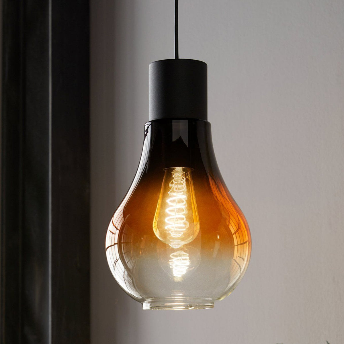 Close-up of a gradient amber and clear glass pendant light with a visible filament.