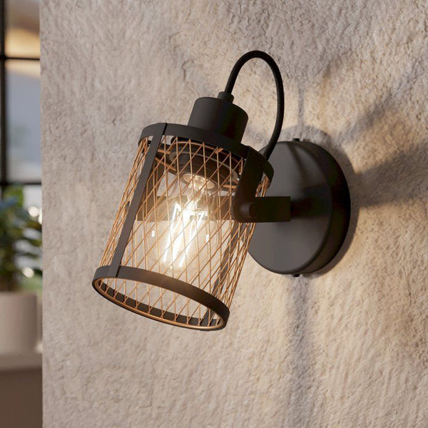 A black industrial-style wall light with a meshed cylindrical shade casting warm light.