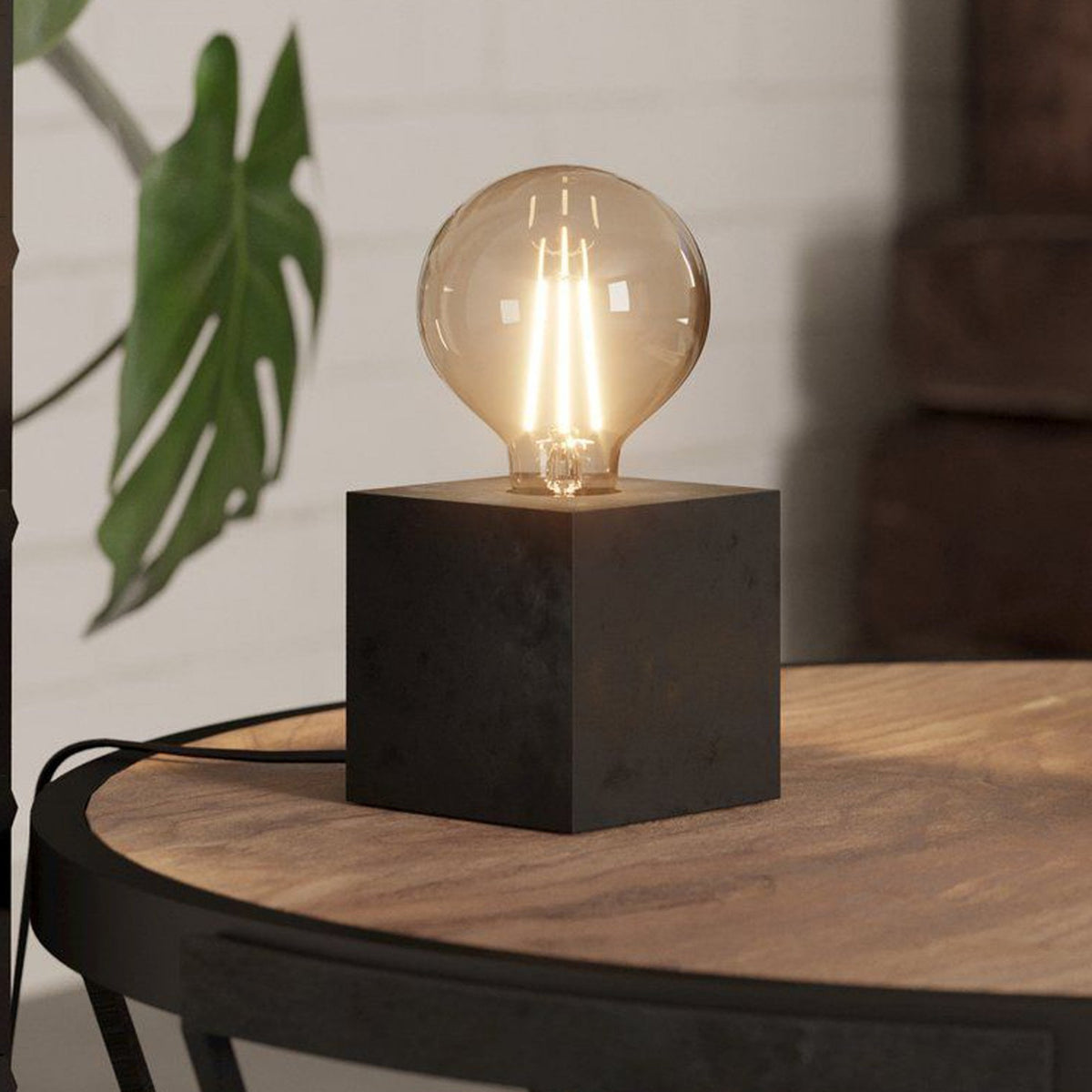 A minimalist table lamp with a dark square base and a large, exposed spherical bulb.