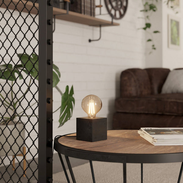 A table lamp with a dark square base and a large, exposed spherical bulb in a living room.
