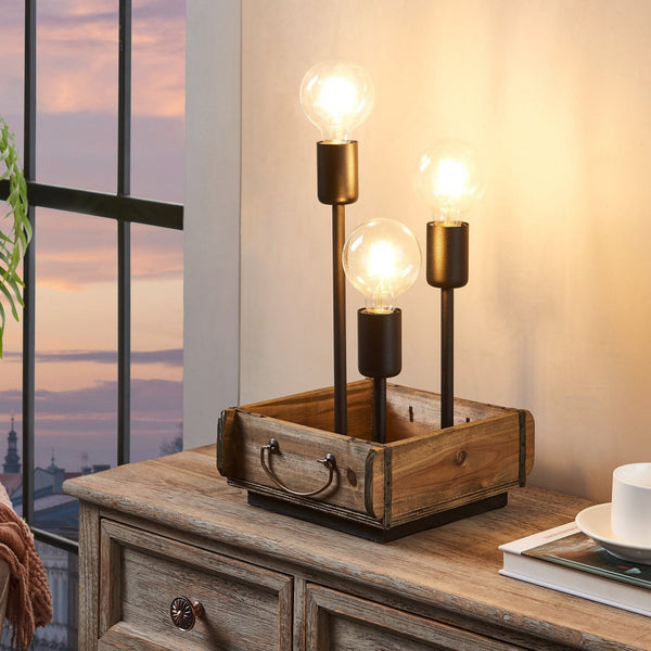 Wooden lamp with three light bulbs on a wooden surface near a window with a sunset view.
