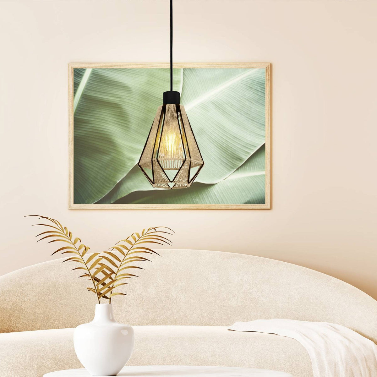 A pendant light hanging above a white sofa, with a framed green leaf print in the background.