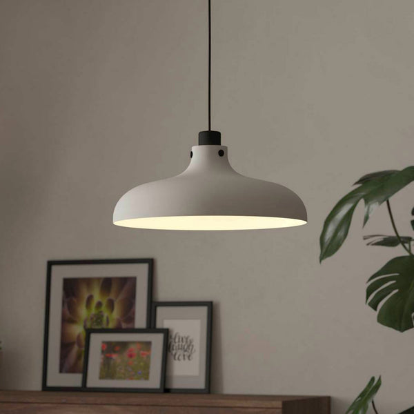 A white pendant light illuminates a cosy room with plants and framed pictures.