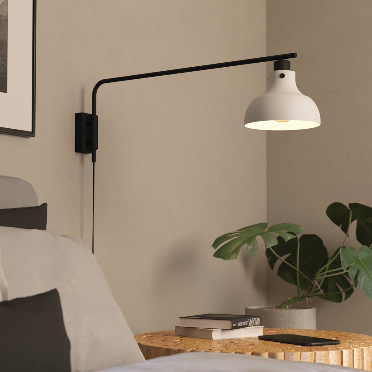 Modern wall-mounted lamp in a bedroom setting with a plant and books on a nightstand.