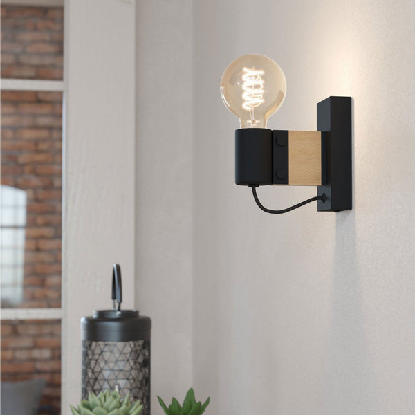 A black and gold wall light with an exposed vintage-style bulb illuminates a modern room.