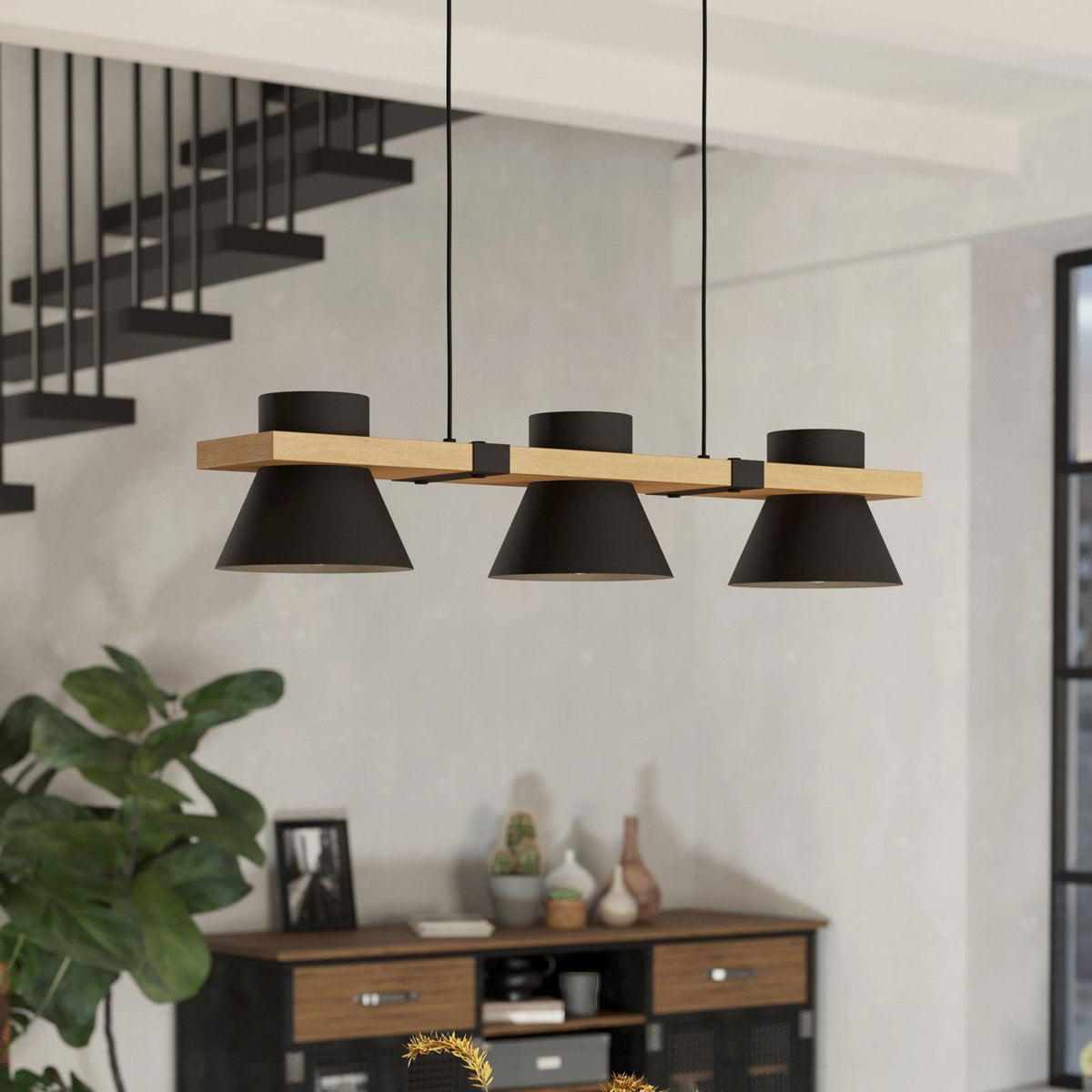 A black and wood pendant light illuminates a dining room with a staircase in the background.