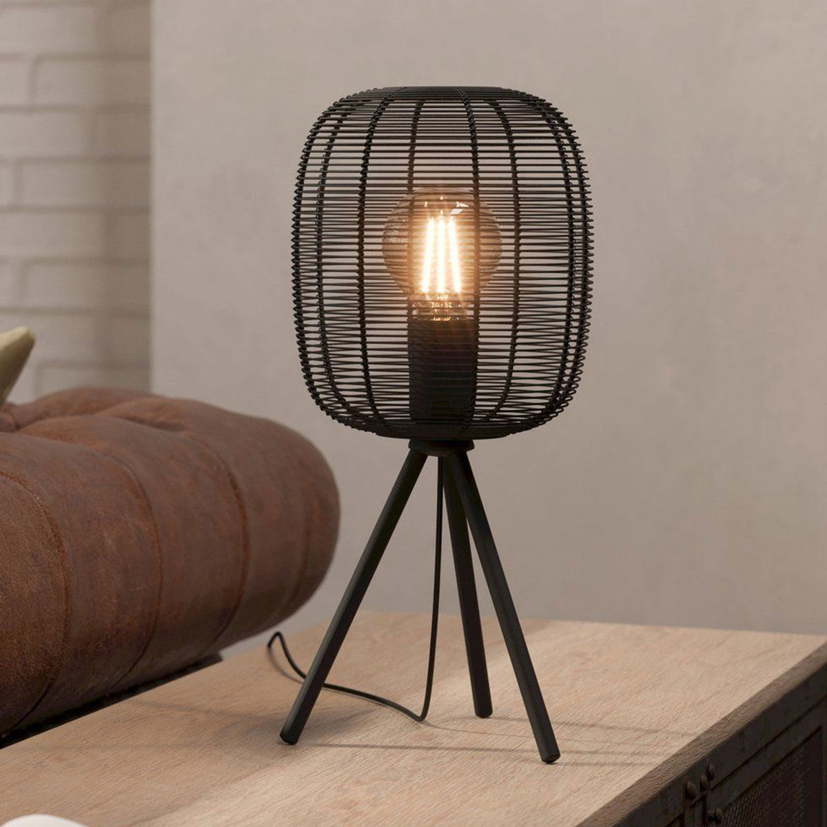 Black metal wire table lamp with tripod legs and exposed bulb, casting a warm glow.