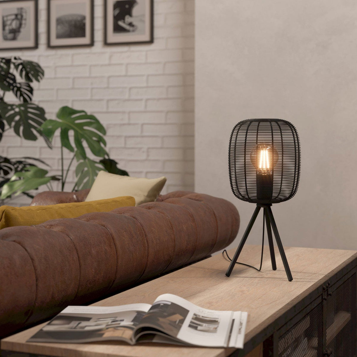 Black metal wire table lamp on a wooden surface in a living room with a brown sofa.