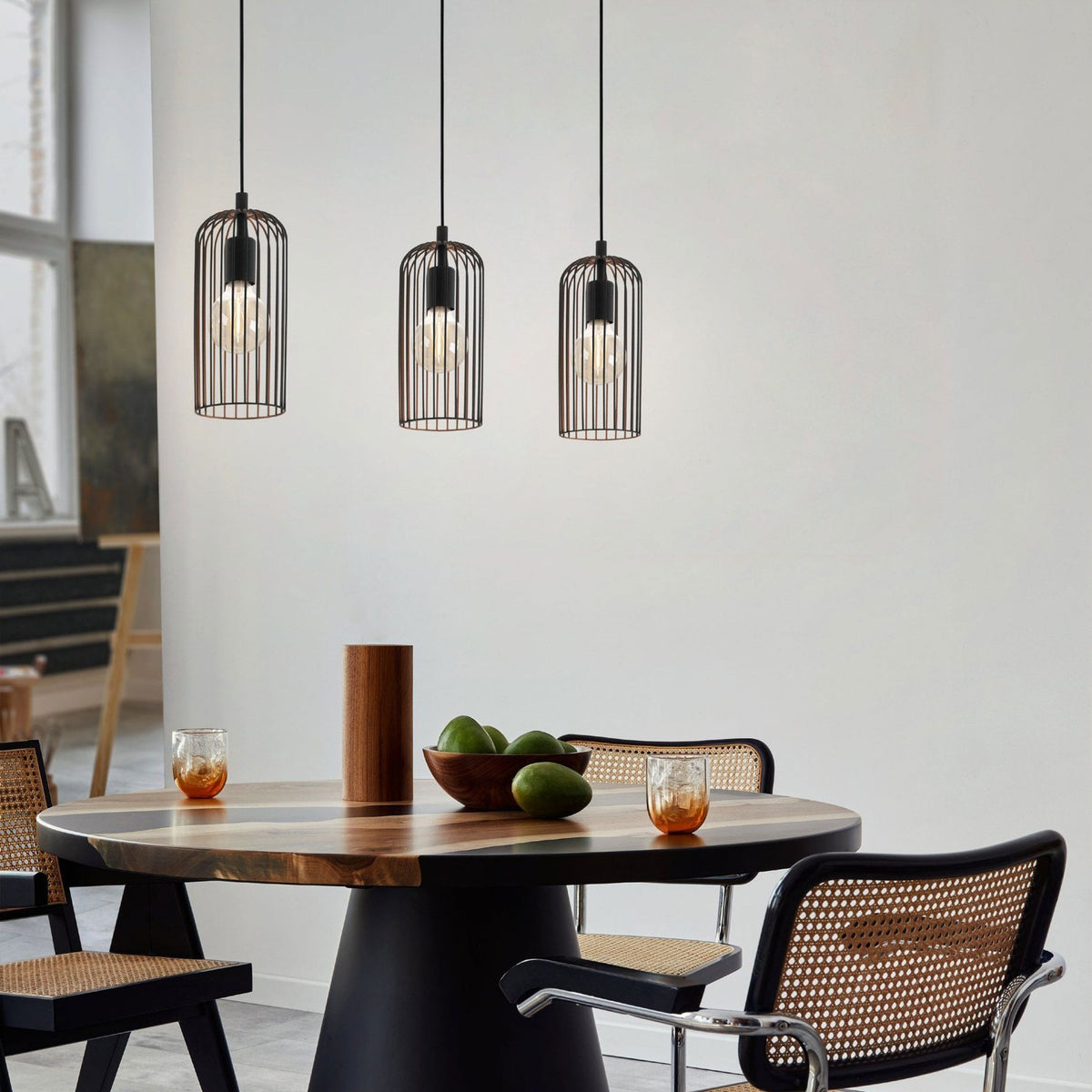 Three caged pendant lights illuminate a stylish dining area with a round table.