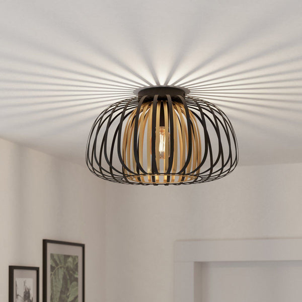 A black wire cage ceiling light with a wooden inner shade casting decorative shadows.