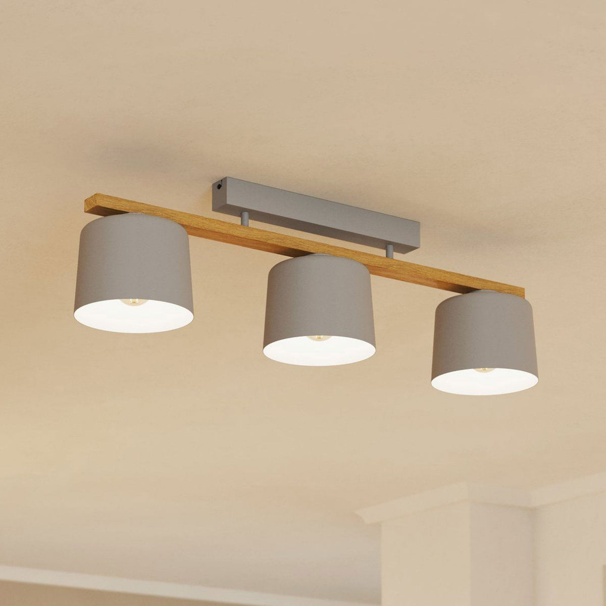 A three-bulb ceiling light with light grey shades and a wooden beam, illuminating a room.