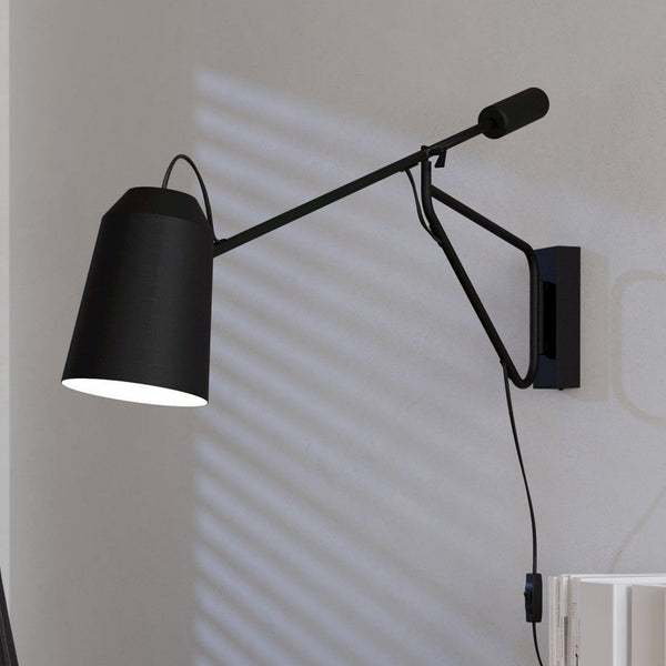 A black wall lamp with an adjustable arm and conical shade illuminating a wall.