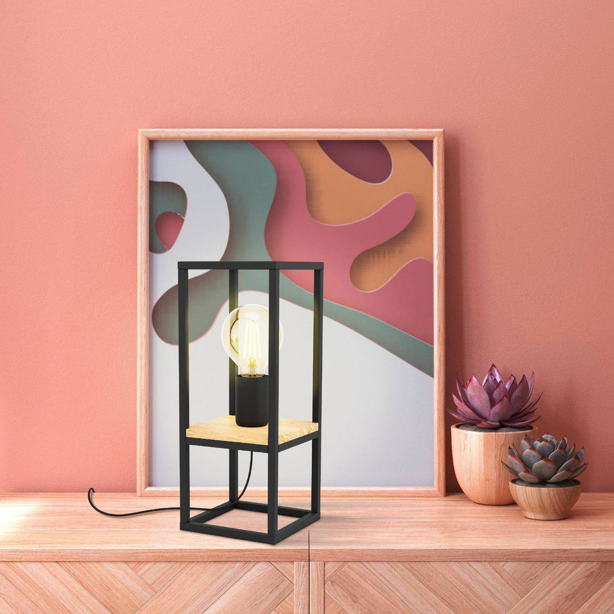 A black framed table lamp with a light wood base on a wooden table.