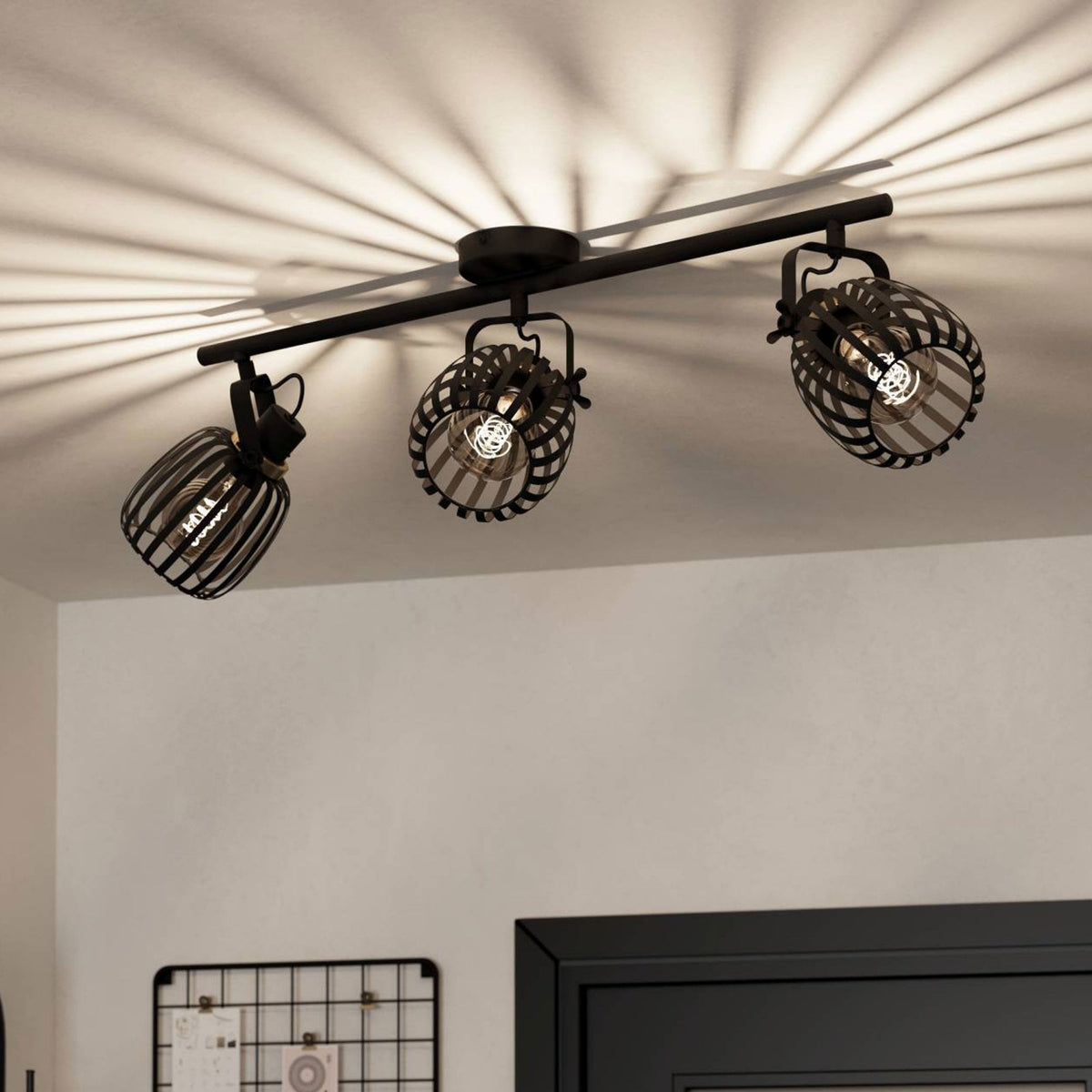 A black three-spot track light casting ribbed shadows on a white ceiling above a doorway.