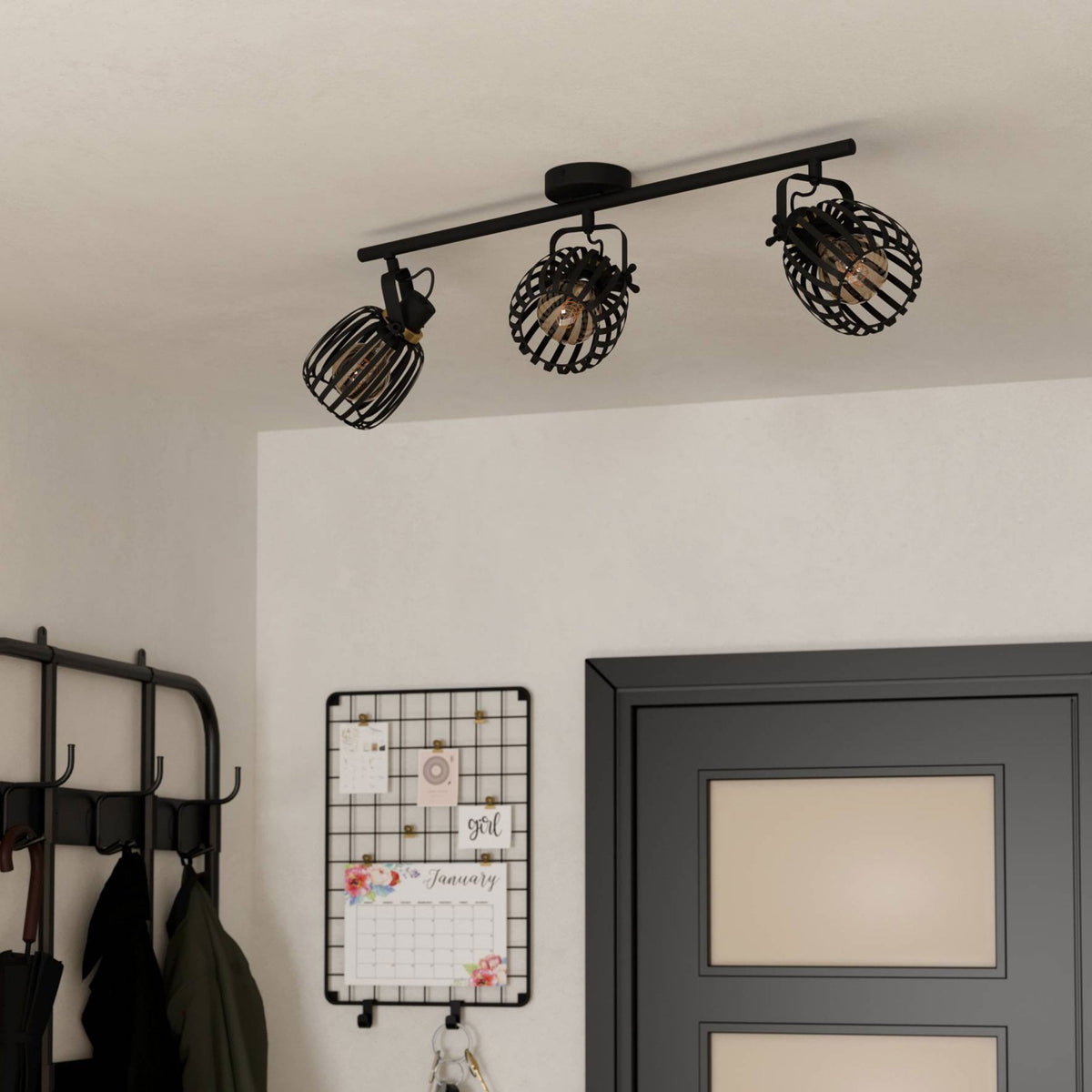 A black three-spot track light installed on a white ceiling above a dark doorway and coat rack.