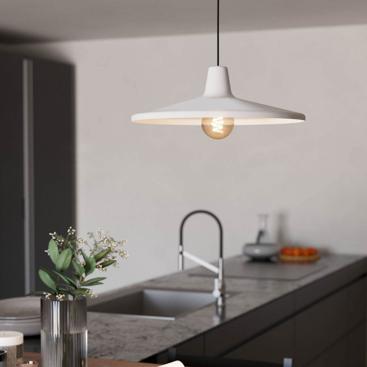 White ceiling lamp with exposed bulb hangs above a kitchen island with a sink and tap.