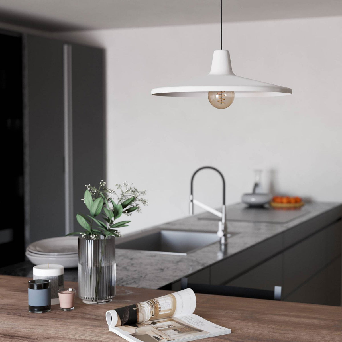 White ceiling lamp with an exposed bulb illuminates a kitchen counter with decor and sink.