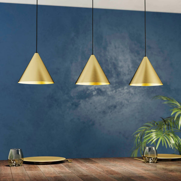 Three brass pendant lights hang over a wooden table set with plates and glasses.