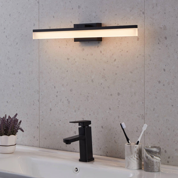 A black rectangular LED bathroom mirror light illuminates a sink with a black tap and toothbrushes.
