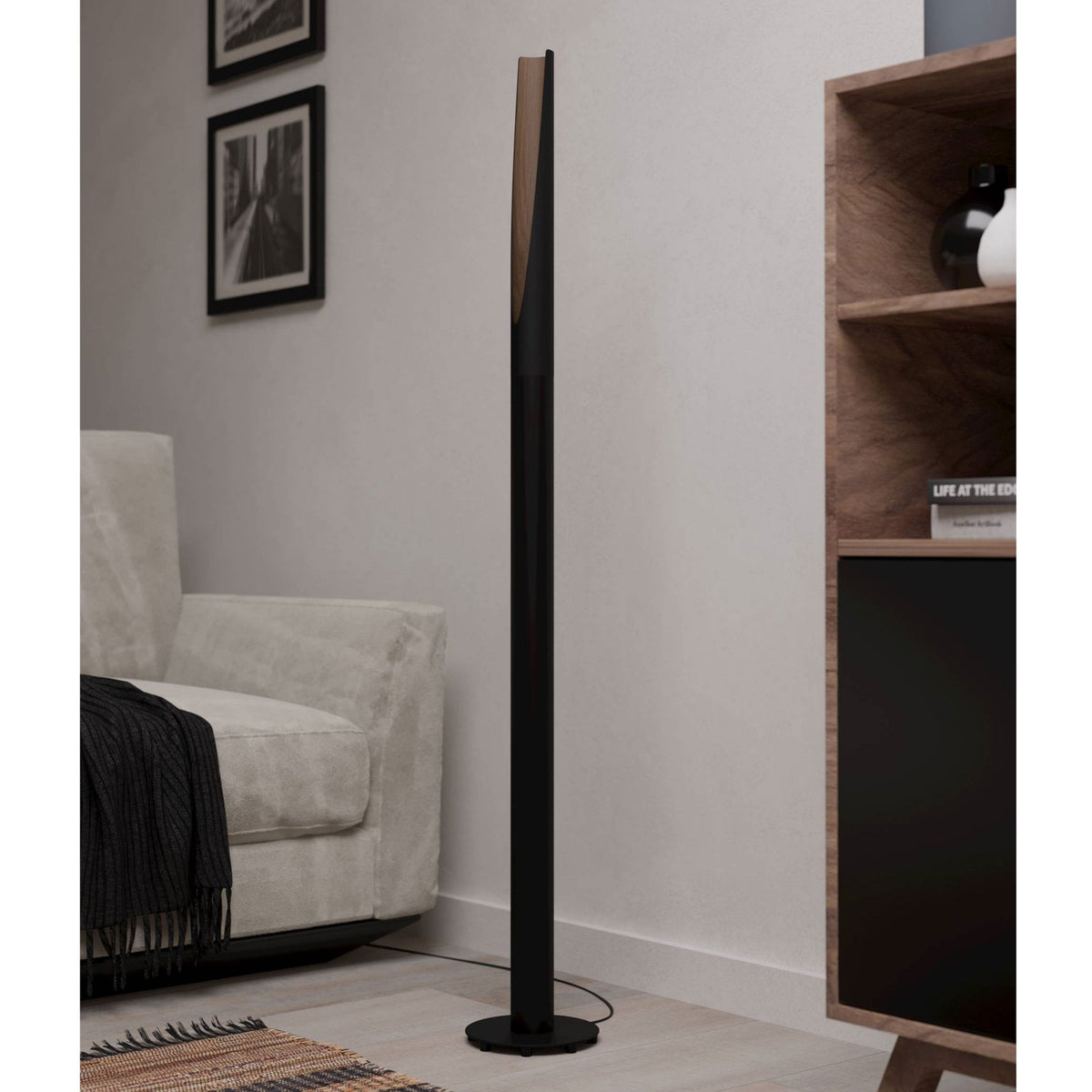 A modern black and wood floor lamp standing in a contemporary living room beside a sofa.