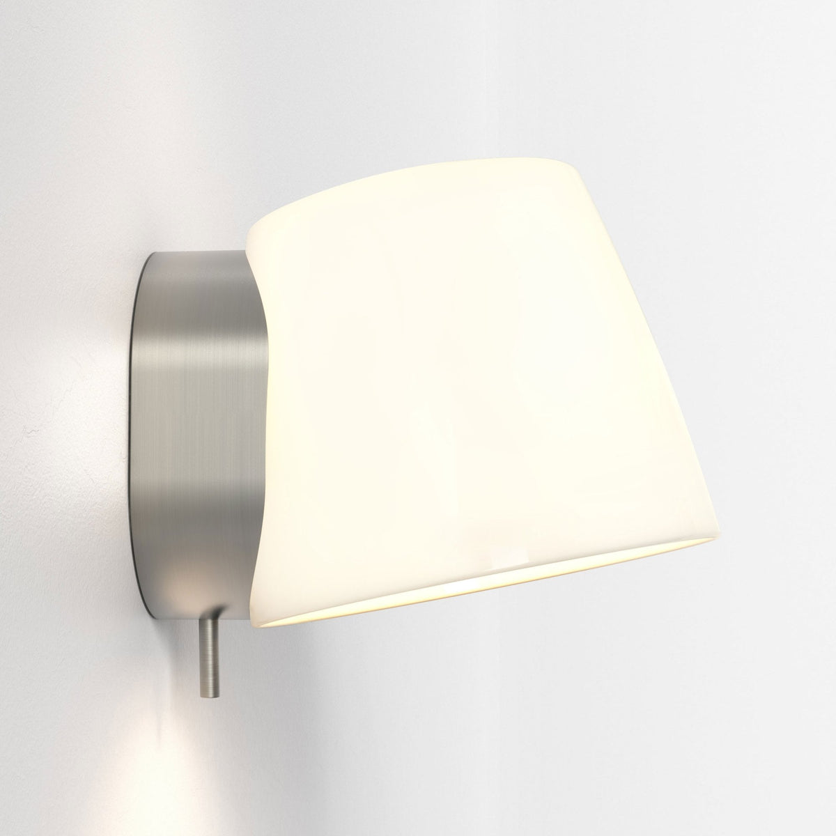Brushed metal wall sconce with a white, curved shade casting a warm glow on a white wall