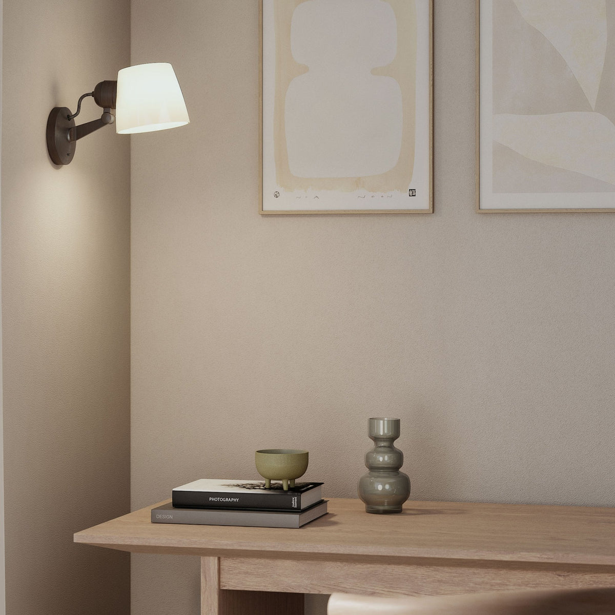 A wall-mounted lamp with a white shade illuminates a light wood table with books and decorative objects