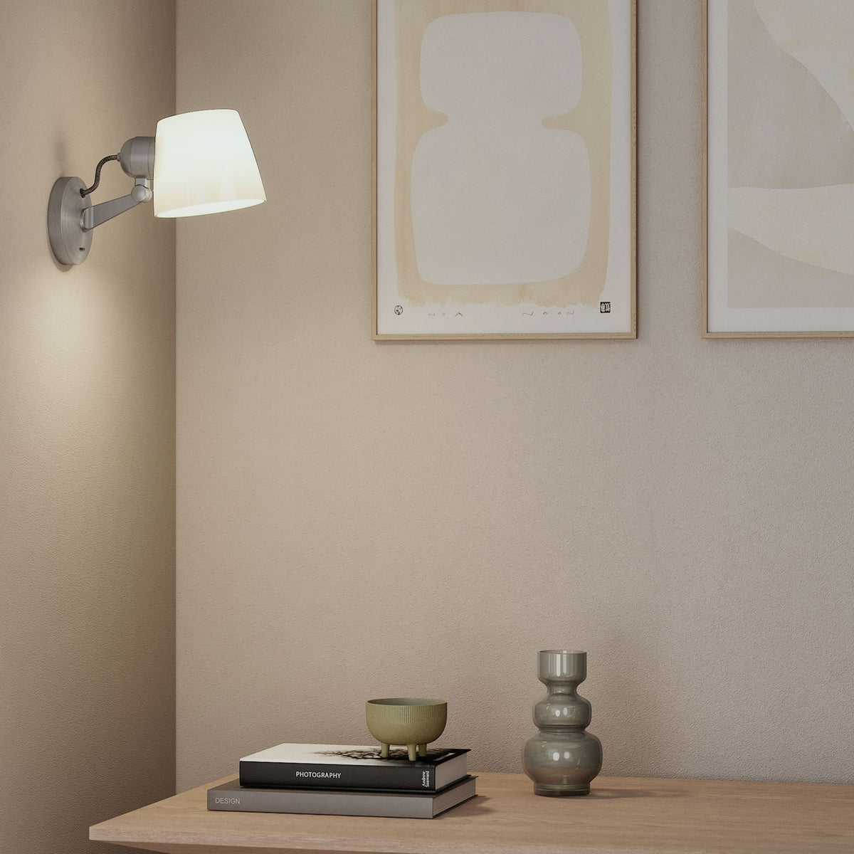 Wall sconce with a white shade and a grey base, illuminating a corner with two framed abstract prints