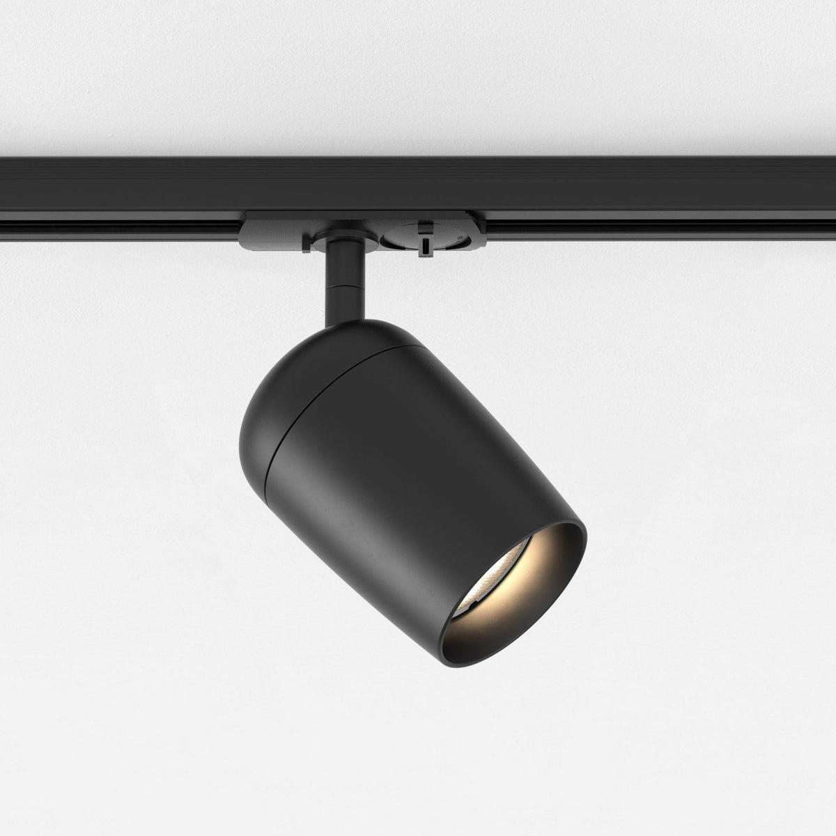 Black track light fixture with a cylindrical head angled downwards, mounted on a black track against a white ceiling